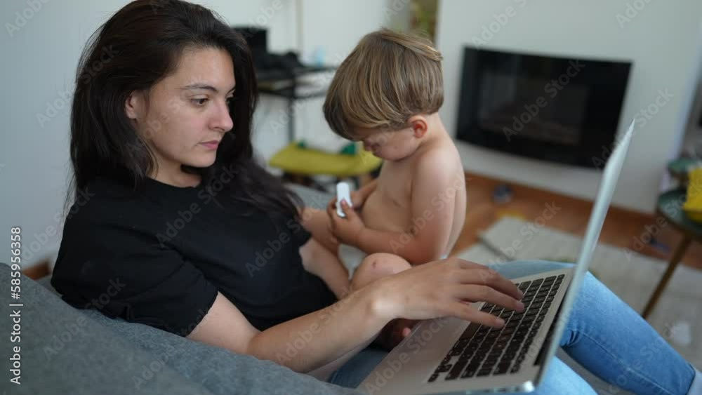 Parent multi tasking in front of laptop computer laying on couch. Toddler baby sitting on mother lap while working from home. Cute modern parenting lifestyle Parent multi tasking in front of laptop computer laying on couch. Toddler baby sitting on mother lap while working from home. Cute modern parenting lifestyle