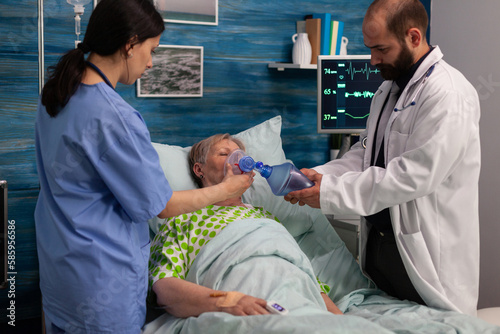 Medical team of a specialized center attending to a chronically ill elderly lady in a hospital room. Woman with respiratory failure being attended by health professionals. photo