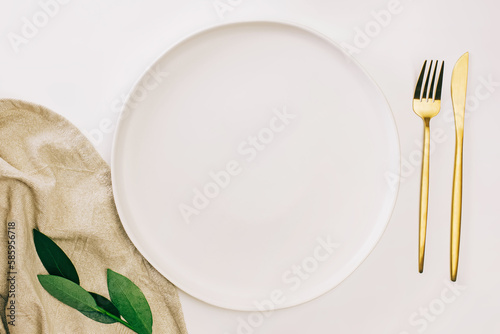 Empty plate and golden cutlery on the white table. Minimalist table setting