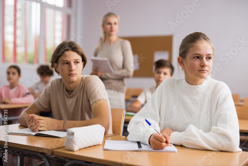 Portrait of teenage school girl and boy sitting together in classroom during lesson in secondary school