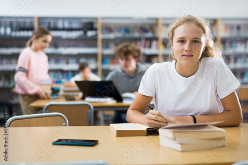 Intelligent female teenager engaged in research working with books in library