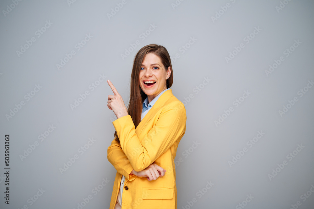 Smiling woman in yellow jacket pointing finger up on gray background