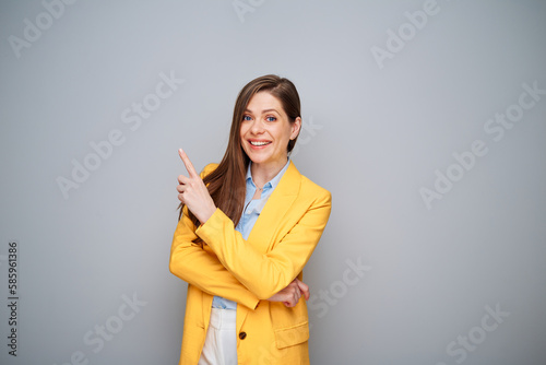 Smiling woman in yellow jacket pointing finger up on gray background