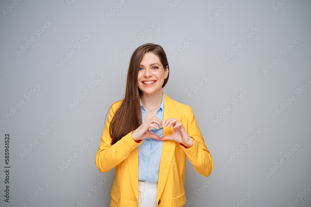 Smiling woman in yellow jacket doing heart shape with fingers on gray background Smiling woman in yellow jacket doing heart shape with fingers on gray background