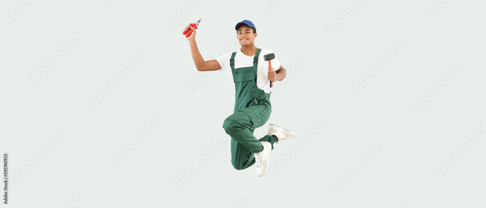 Jumping African-American young man in uniform and with tools on light background