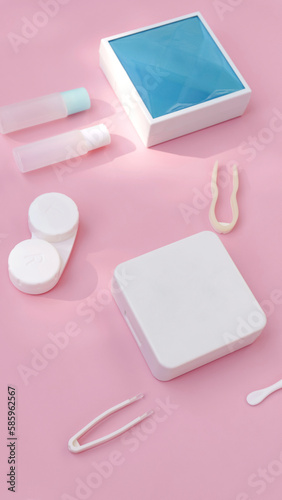 lenses, a container for lenses, tweezers and a small mirror lie on a pink background. contact lens tools