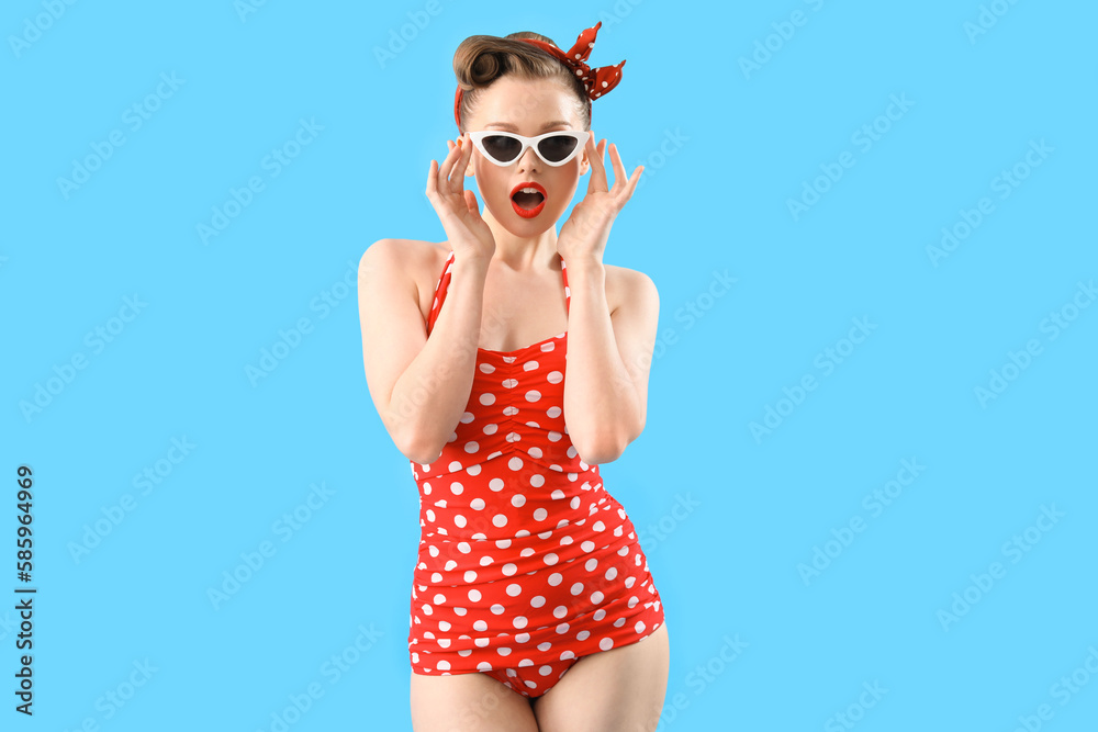 Shocked young pin-up woman in polka dot swimsuit on blue background Shocked young pin-up woman in polka dot swimsuit on blue background