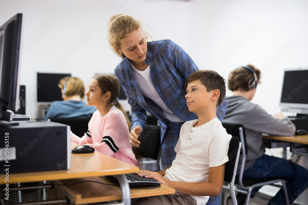 Teenager girl helping younger boy with computer trouble in computer classroom.