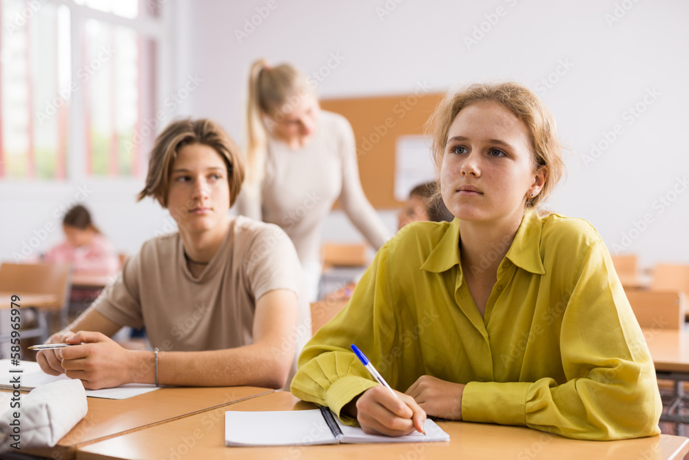 Fototapeta premium Portrait of teenage school girl and boy sitting together in classroom during lesson in secondary school