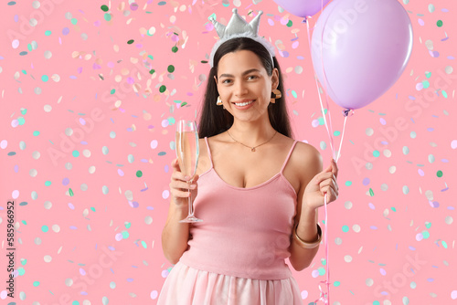 Happy young woman with glass of champagne and balloons celebrating Birthday on pink background