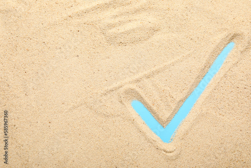 Check mark made of sand on blue background