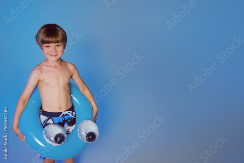 Happy cute boy 6 years old with a life buoy at the blue background