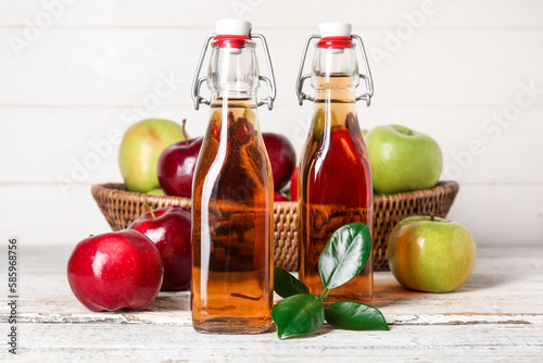 Glass bottles of fresh apple cider vinegar and basket with fruits on white wooden table