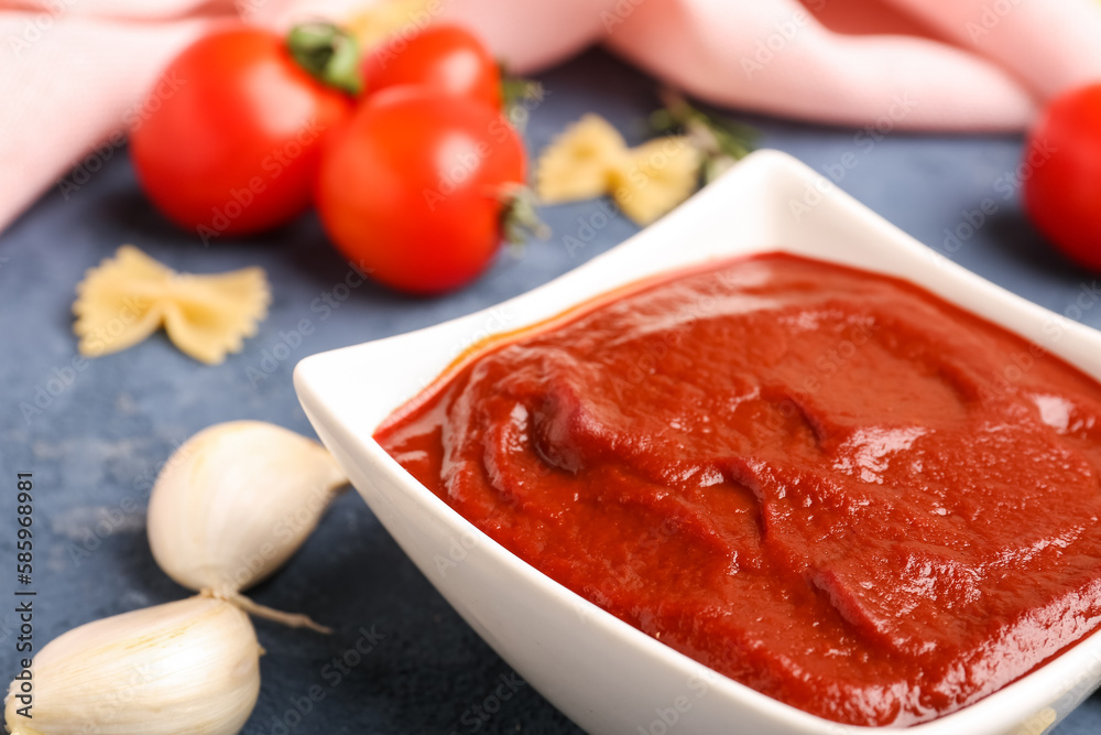 Bowl of tasty tomato paste, garlic cloves and raw farfalle pasta on grey grunge background Bowl of tasty tomato paste, garlic cloves and raw farfalle pasta on grey grunge background