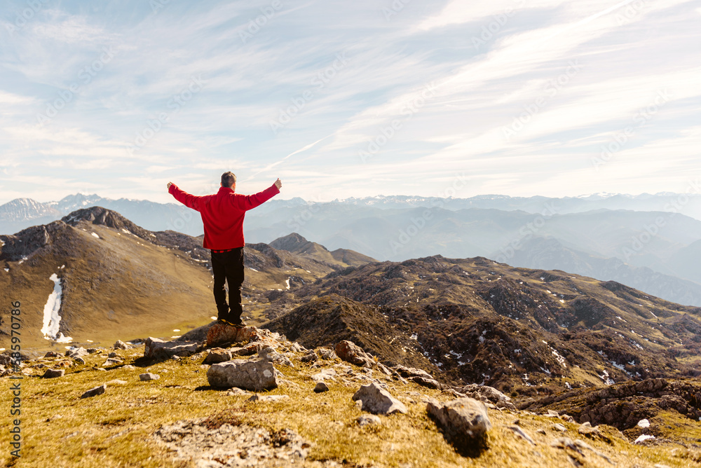 Obraz premium man on his back in red clothes and arms raised contemplating the mountain landscape after hiking up a mountain. sport, travel and adventure.