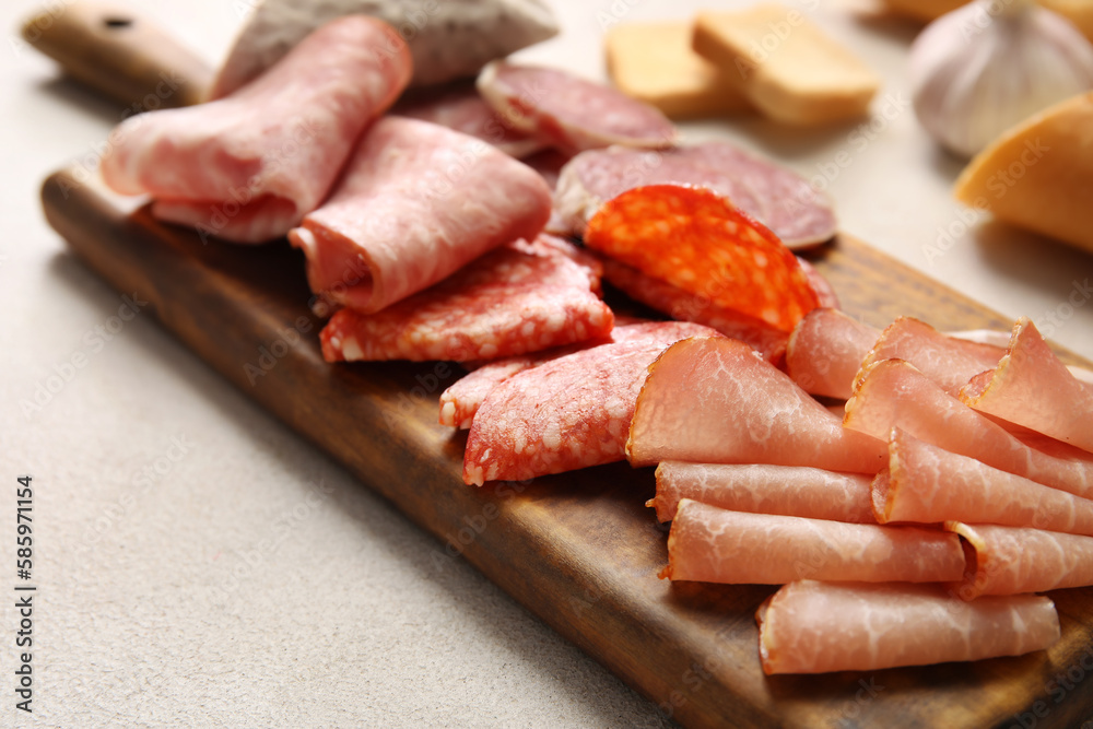 Wooden board with assortment of tasty deli meats on light background, closeup Wooden board with assortment of tasty deli meats on light background, closeup