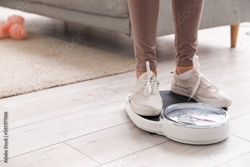 Tablou pe pânză Sporty mature woman measuring her weight on scales at home, closeup