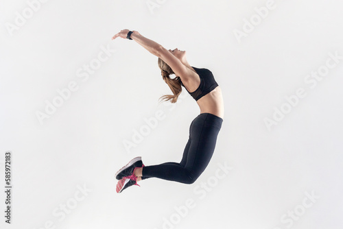 Portrait of athletic blonde woman with perfect body jumping high and keeping hands up, hands up.