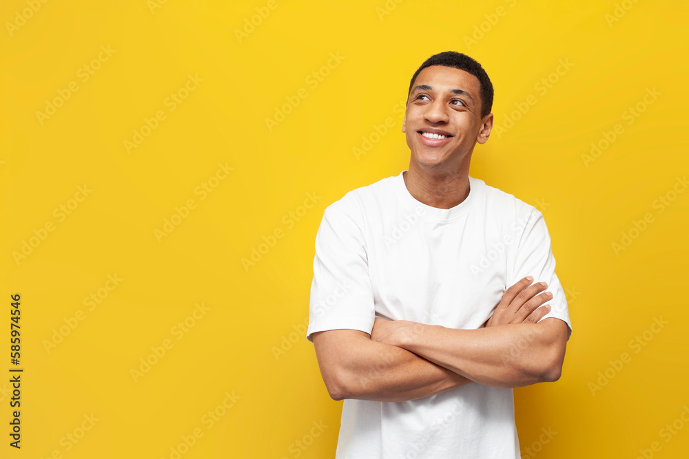young pensive afro american guy in white oversized t-shirt stands on yellow isolated background and looks to the side