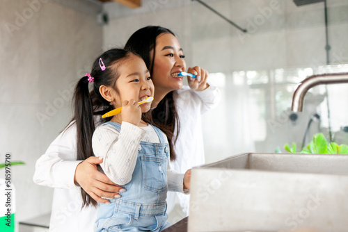 asian little girl with mom brushing teeth in bathroom, korean woman helping to brush daughter's teeth at home together