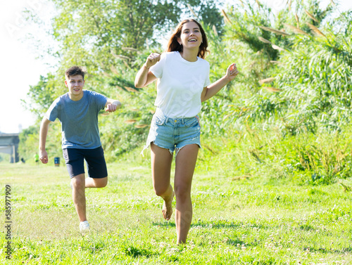 Laughing teenagers playing outdoors funning at grass on summer day