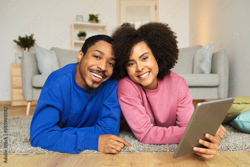 Black Couple Using Digital Tablet Smiling To Camera At Home