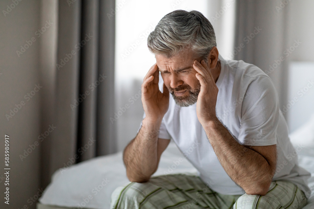 Middle aged man sitting on bed, touching his head Middle aged man sitting on bed, touching his head