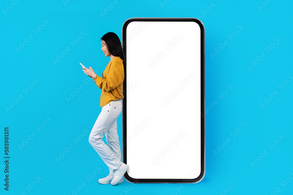 Smiling asian woman standing by big phone, using app Smiling asian woman standing by big phone, using app