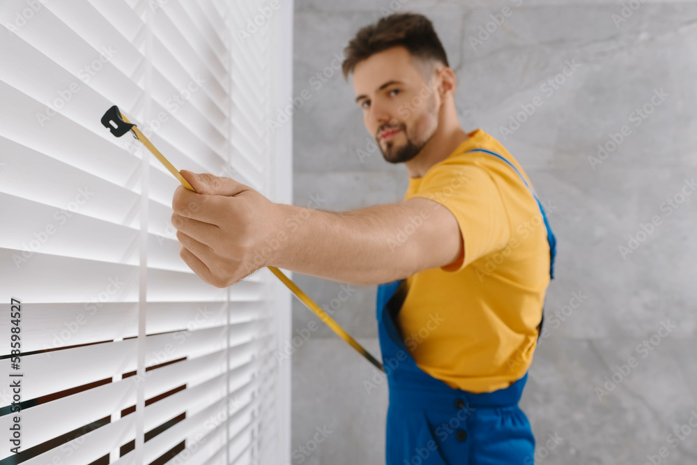 Worker in uniform using measuring tape while installing horizontal window blinds indoors, focus on hand Worker in uniform using measuring tape while installing horizontal window blinds indoors, focus on hand