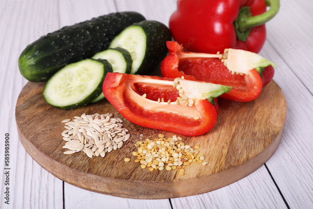 Fresh cucumbers, red bell peppers and vegetable seeds on white wooden table, closeup