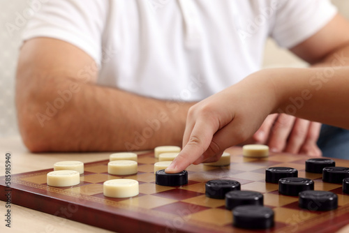 Father playing checkers with his son at table in room, closeup