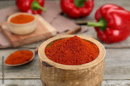 Bowl with aromatic paprika powder on wooden table, closeup