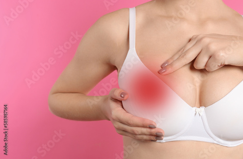 Woman checking her breast on pink background, closeup