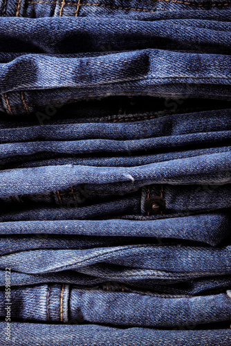 Worn denim trousers. Machine stitch close up. Denim texture in blue. The concept of repairing old clothes. Sewing factory. Fashionable aging clothes. Stack of jeans. 