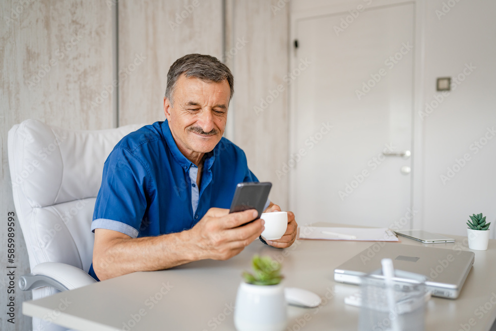senior man hold cup of coffee and mobile phone while sitting at work senior man hold cup of coffee and mobile phone while sitting at work