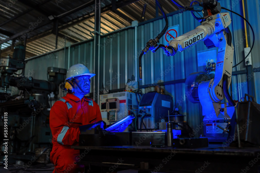 Engineer monitors and controls automatic welding robotic arm machine in intelligent automotive factory with industry 4.0 digital manufacturing execution system software monitoring.