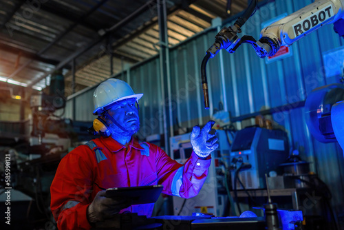 Engineer monitors and controls automatic welding robotic arm machine in intelligent automotive factory with industry 4.0 digital manufacturing execution system software monitoring.