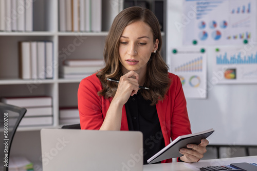 Young latin professional business woman office worker analyst sitting at desk working on laptop thinking on project plan, analyzing marketing or financial data online, Financial and Accounting concept