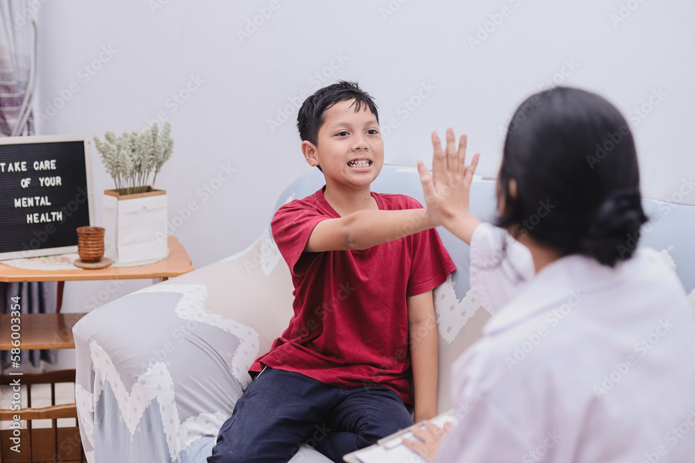 School boy making high five to professional female psychologist at the office, feeling better after therapy. Children's mental health.