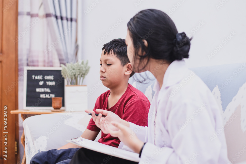 Professional female child psychologist working with sad school boy in a office. Woman makes notes on paper. Children's mental therapy.