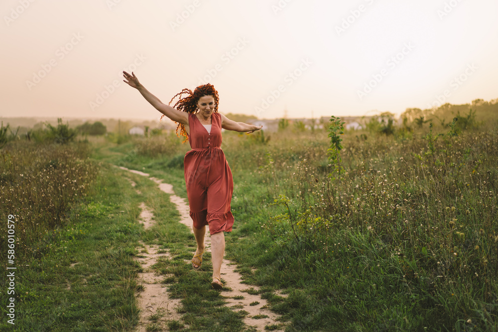 Portraits of a charming red-haired woman with a cute face. Girl posing for the camera in the field at sunset. Portraits of a charming red-haired woman with a cute face. Girl posing for the camera in the field at sunset.