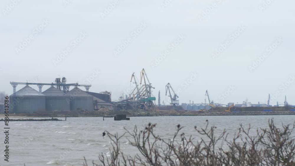Distant view busy working port cranes at Port of Liepaja, large dry-cargo ships docked, overcast day, moody scenic view, wide shot Distant view busy working port cranes at Port of Liepaja, large dry-cargo ships docked, overcast day, moody scenic view, wide shot