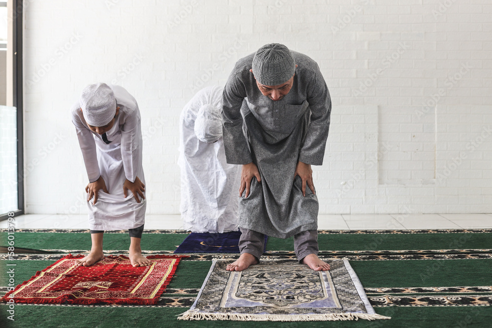 Asian muslim family are kneeling and praying salah together at mosque ...
