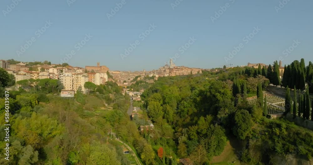 Aerial Forward Shot Of Buildings Amidst Trees With Cars On Road Under Clear Sky During Sunny Day - Siena, Italy Aerial Forward Shot Of Buildings Amidst Trees With Cars On Road Under Clear Sky During Sunny Day - Siena, Italy