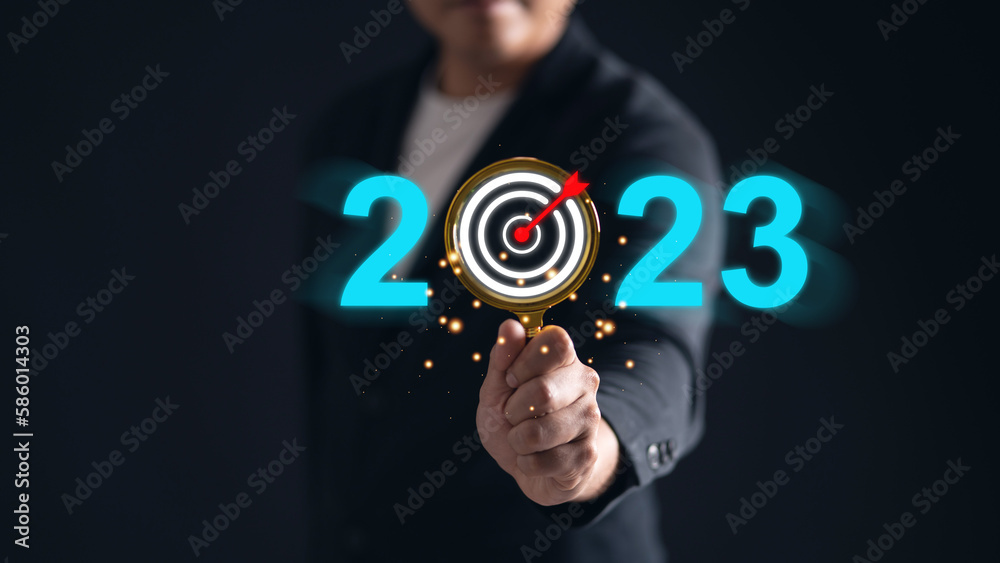 Man using his hand holding a magnifying glass with an arrow target icon in the number 2023 Man using his hand holding a magnifying glass with an arrow target icon in the number 2023
