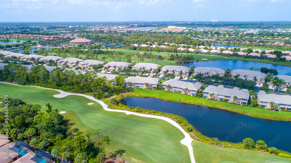 Fototapeta premium Golf Community Aerial View from Drone with Florida Real Estate Surrounded by Landscaping, Lakes, and the Gulf of Mexico in the Background