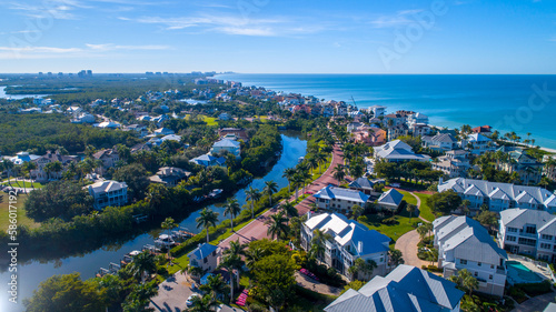 Aerial Perspective from Drone Featuring the Barefoot Beach in Bonita Springs, Florida. Blue Water Coastline with Clear Sky and Wispy Clouds in the Background and Clusters of Homes in the Foreground
