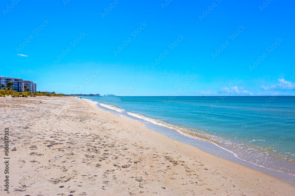 Beachside View of Ocean Waves with White Sand and Island Foliage in the Background Featuring a Clear Blue Sky 