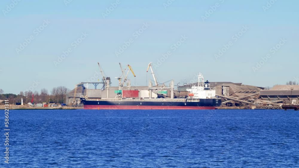 Timelapse view of busy working port cranes at Port of Liepaja, large dry-cargo ships docked, sunny day, moody scenic view, Baltic sea in foreground, wide shot zoom in Timelapse view of busy working port cranes at Port of Liepaja, large dry-cargo ships docked, sunny day, moody scenic view, Baltic sea in foreground, wide shot zoom in