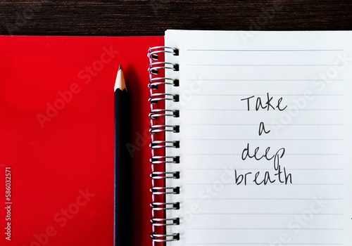 Pencil on red notebook with hand written text TAKE A DEEP BREATH, concept of to pause for a moment to compose or calm oneself, act of exhaling is thought to promote calmness